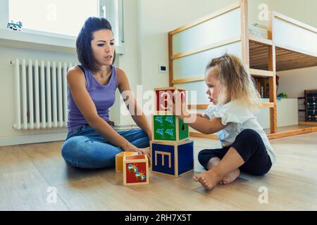 Collant sur des jouets en bois, une mère et sa fille blonde chérissent des moments d'apprentissage ludiques dans la chambre de l'enfant Banque D'Images