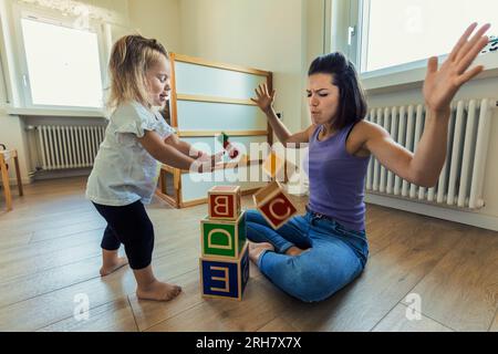 La fille blonde et la mère apprécient le temps de jeu avec des jouets en bois dans la chambre à coucher, grandissant ensemble dans le plaisir et le lien éducatif Banque D'Images