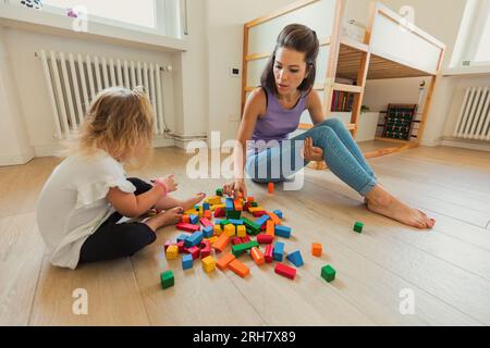 Dans la salle de jeux, une mère et son enfant blond explorent des jouets en bois, apprennent et rient, favorisent la créativité et le lien Banque D'Images