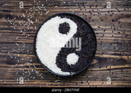 Riz Nerone, noir interdit biologique, et riz au jasmin dans un bol noir sur fond de bois en forme de Yin Yang. Vue à plat du dossier de la table. Banque D'Images