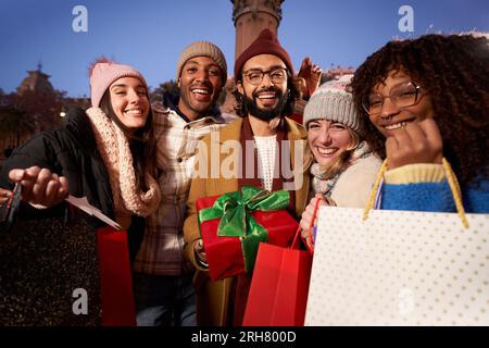 Portrait groupe souriant personnes multi-ethniques montrant des sacs d'hiver de Noël cadeaux à l'appareil photo. Banque D'Images