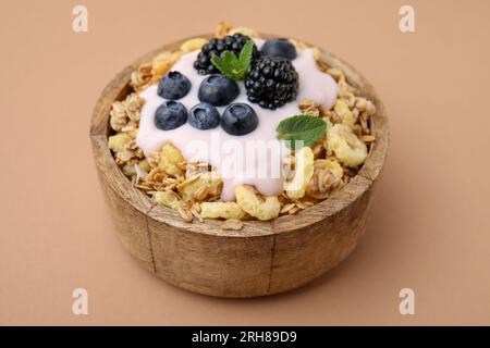 Granola savoureux, yaourt et baies fraîches dans un bol sur fond brun pâle, gros plan. Petit déjeuner sain Banque D'Images