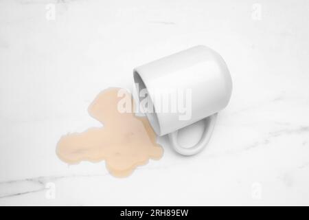 Flaque de liquide et tasse renversée sur table en marbre blanc, vue de dessus Banque D'Images