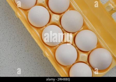 Œufs blancs parfaitement logés dans un carton jaune, prêts à l'emploi culinaire. Banque D'Images