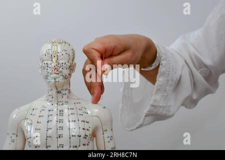 Une main de femme enfonçant une aiguille d'acupuncture dans un mannequin humain, apprenant et pratiquant l'acupuncture. Banque D'Images