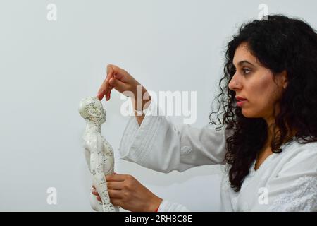 Femme enfonçant une aiguille pour acupuncture dans un mannequin humain. Banque D'Images