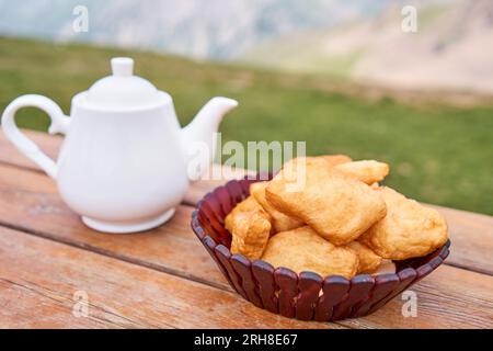 Théière avec thé et délicieuses pâtisseries nationales kazakhes baursak. Café de rue dans les hauts plateaux avec vue sur les montagnes.. Faites frire la pâte dans l'huile bouillante Banque D'Images