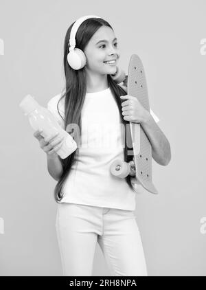 Jeune fille d'école avec planche à roulettes sur fond isolé de studio. Printemps écofille tendance, urbain style adolescent. Joyeux portrait d'adolescent. Fille souriante. Banque D'Images