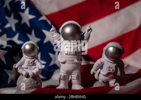 Trois jouets en plastique figurent astronaute sur le drapeau américain arrière-plan espace de copie. 50th anniversaire des États-Unis atterrissage sur la Lune concept de voyage hors terre, vols commerciaux privés de spaceman. Missions spatiales et durabilité Banque D'Images
