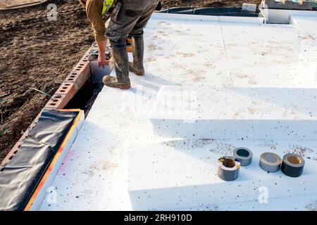 Constructeur plaçant des panneaux isolants de polystyrène sur la membrane d'étanchéité pendant la construction de plancher. Concept d'économie d'énergie Banque D'Images