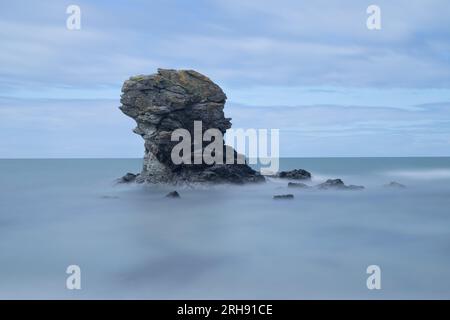 Petite pile rocheuse juste à côté d'une plage de galets au pays de Galles. Une longue exposition donne à la mer un aspect soyeux lisse. Banque D'Images