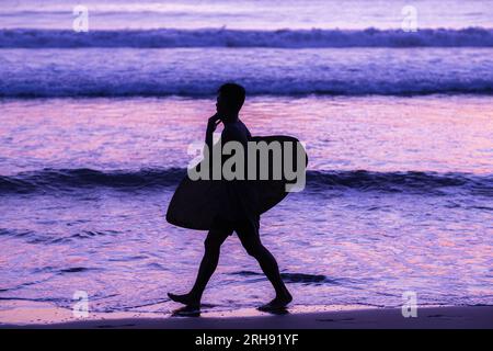 Silhouette de surfeurs portant leur planche de surf sur la plage de coucher du soleil avec des vibrations violettes Banque D'Images