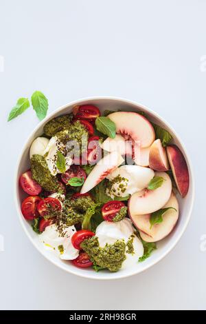 Salade burrata d'été avec pêches, tomates cerises, pesto et épices dans un bol sur fond blanc, vue de dessus. Banque D'Images