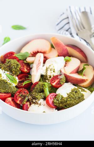 Salade burrata estivale avec pêches, tomates cerises, pesto et épices dans un bol sur fond blanc, gros plan. Banque D'Images