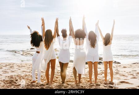 Fête de poule sur la plage. Vue arrière d'un groupe de diverses dames marchant par le bord de la mer, tenant et levant la main Banque D'Images