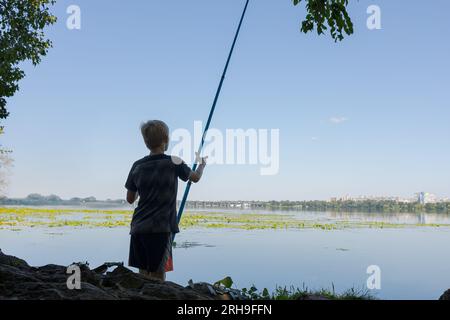 Un adolescent se prépare à aller pêcher sur la rivière. Pêche sportive sur la rivière en été. Banque D'Images