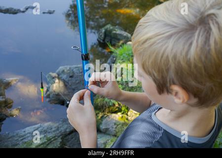 Dans les mains de l'adolescent est l'appât qu'il met sur le crochet. Pêche sportive sur la rivière en été. Banque D'Images