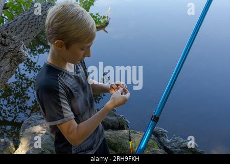 Le pêcheur adolescent vérifie l'appât et en met un nouveau. Pêche sportive sur la rivière en été. Banque D'Images