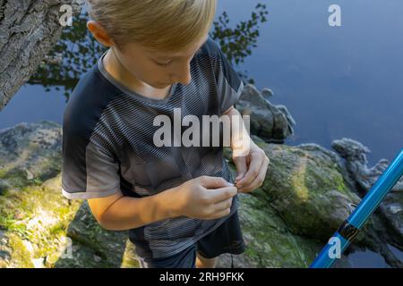 Le pêcheur adolescent vérifie l'appât et en met un nouveau. Pêche sportive sur la rivière en été. Banque D'Images