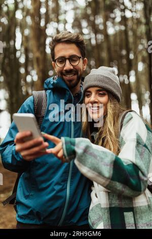 Joyeux jeune couple caucasien dans des vestes dans la forêt Profitez des vacances de voyage, utilisez la carte de l'application smartphone Banque D'Images