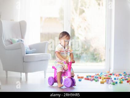 Adorable bébé asiatique sur petit vélo de poussée à la maternelle ou à la garderie. Enfant jouant avec des jouets éducatifs colorés dans la maternelle. Banque D'Images