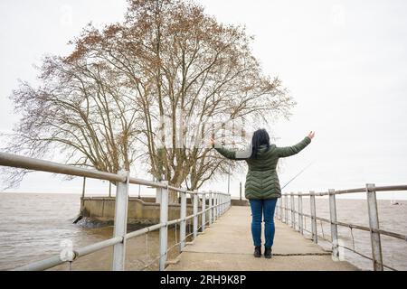 Jeune femme latine à bras ouverts debout au milieu de la jetée sur la rivière dans le port d'Olivos à Buenos Aires, concept de voyage, espace de copie. Banque D'Images