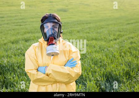 Personne en combinaison et masque à gaz appel pour sauver la planète tout en se tenant sur le champ vert au coucher du soleil. Banque D'Images