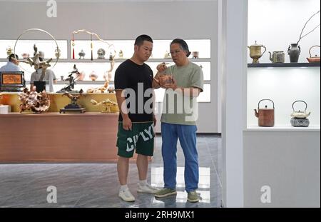 (230815) -- NANCHANG, 15 août 2023 (Xinhua) -- Huang Junjun (à droite) s'entretient avec un visiteur dans un hall d'exposition d'œuvres d'art gravées sur cuivre dans sa société de Guixi City, province de Jiangxi dans l'est de la Chine, 9 août 2023. Gravure sur cuivre, ou sculpture sur cuivre, un métier d'utilisation de couteaux pour sculpter des motifs sur des marchandises en cuivre, a une histoire d'environ 1 000 ans. En 2021, la gravure sur cuivre Guixi a été répertoriée comme l'un des patrimoines culturels immatériels au niveau national. L'artisanat a besoin de plus de 150 types différents de couteaux et une douzaine de compétences de sculpture pour créer une œuvre d'art complète, et la vaisselle en cuivre doit passer par dessus Banque D'Images