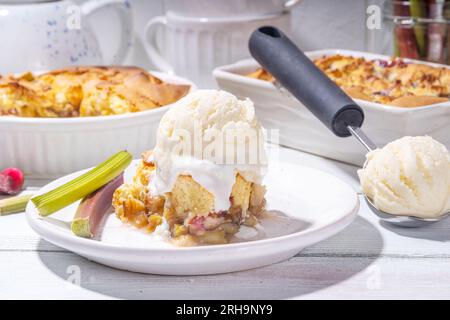 Tarte parée à la framboise aux baies, gâteau maison à l'éponge avec rhubarbe sucrée et fraise, servi avec boule de glace à la vanille, sur un k en bois blanc ensoleillé Banque D'Images