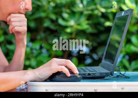 Femme travaillant en ligne à l'aide d'un ordinateur portable tout en étant assis sur la table de camping devant la tente. Concept de travail à distance et de camping dans la nature. Banque D'Images