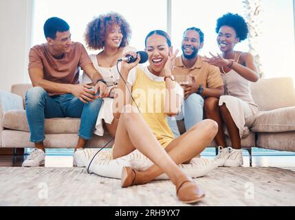Microphone, heureux ou amis chantant dans le salon à la maison ensemble dans une fête sur les vacances de vacances. Chanteuse fille, hommes ou groupe de femmes drôles Banque D'Images