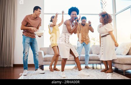 Chant, musique et amis faisant du karaoké dans le salon avec microphone à playlist ou radio. Heureux, diversité et jeunes dansant, liant Banque D'Images