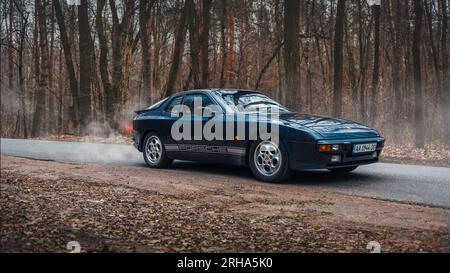 Porsche 944 bleu foncé dans la forêt d'automne. Vue de trois quarts avant de la voiture de sport des années 1980. Banque D'Images