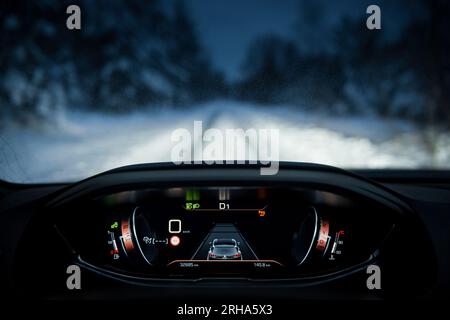 Vue à la première personne de conduire Peugeot 3008 à travers la forêt d'hiver. Dahboard, groupe de jauges au point et route enneigée et arbres en arrière-plan Banque D'Images