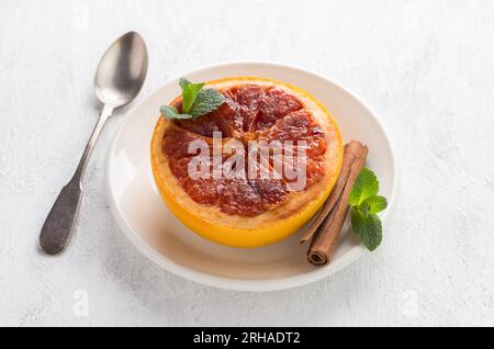 Pamplemousse cuit au four avec cassonade et cannelle garnie de menthe sur fond gris clair. Délicieux dessert de régime sain ou petit déjeuner. Banque D'Images