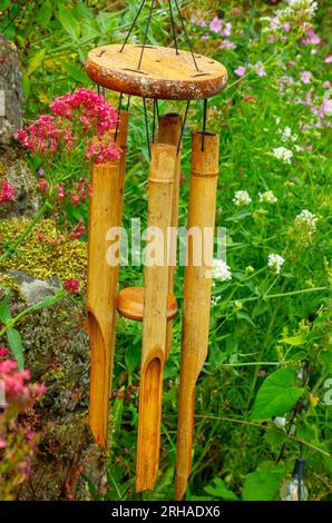 Carillons de vent en bois suspendus à l'extérieur dans un jardin avec des fleurs visibles en arrière-plan. Banque D'Images