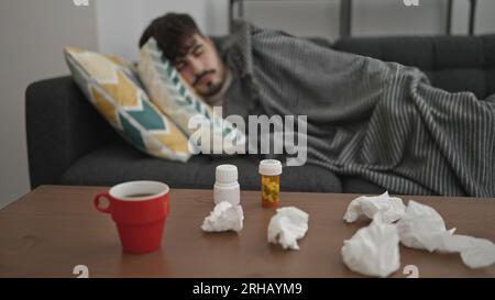 Jeune homme hispanique allongé sur le canapé malade avec des mouchoirs et des pilules sur la table à la maison Banque D'Images