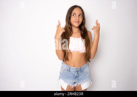 Enfant adolescent tenant les doigts croisés pour la bonne chance. Portrait de fille joyeuse prie et espère que les rêves deviennent réalité, croise les doigts pour la bonne chance, isola Banque D'Images