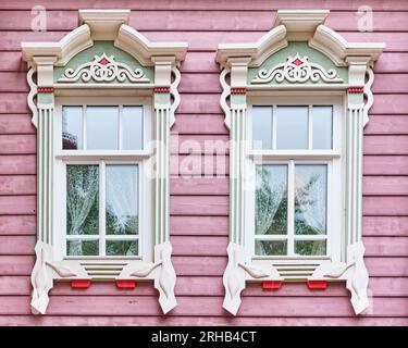 Typique deux fenêtres en bois avec architraves sculptées sur façade de promenade rose de tatar recréé maison résidentielle début 20e siècle. Vieux Tatar Settlem Banque D'Images