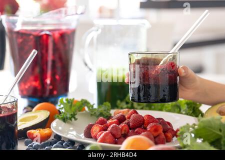 Un verre de smoothie de baies dans la main d'un enfant à la maison dans la cuisine. Banque D'Images