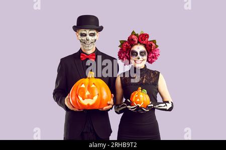 Couple heureux habillé en costumes de squelette tenant des citrouilles d'Halloween et souriant Banque D'Images