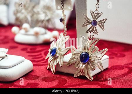 Gros plan de bijoux en filigrane d'argent - boucles d'oreilles en forme de croix maltaise avec des pierres précieuses en saphir bleu brillant poli incrustées au milieu Banque D'Images