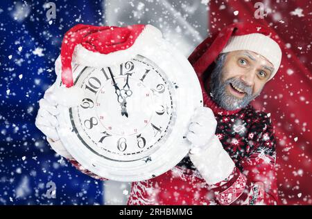 Le Père Noël tient une horloge dans ses mains, sur laquelle il reste 5 minutes jusqu'à la nouvelle année, Noël, sur fond du drapeau de . Nouvel an an an Banque D'Images