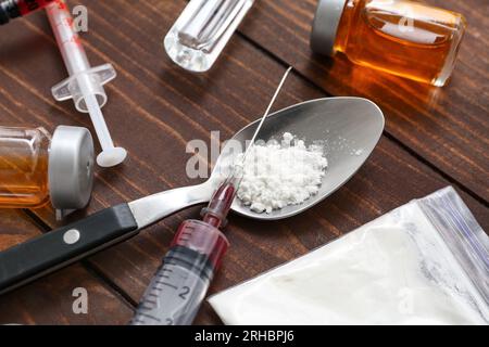 Cuillère avec des médicaments, des ampoules et des seringues sur fond de bois, gros plan Banque D'Images
