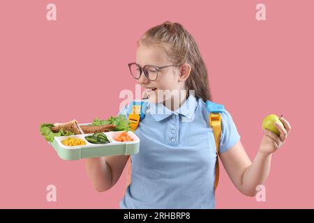 Petite fille heureuse avec sac à dos, Lunchbox et pomme sur fond rose Banque D'Images