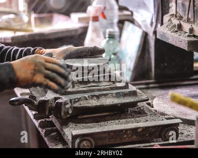 Crop anonyme artisan versant de l'argile bleue sèche dans le moule pour fabriquer des carreaux de céramique faits à la main dans le studio de poterie Banque D'Images