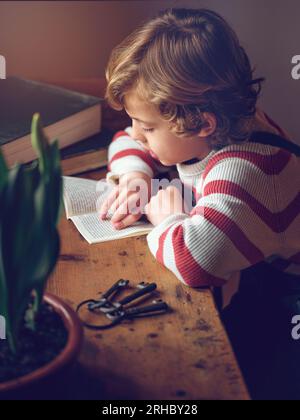 De dessus vue latérale de mignon petit enfant focalisé livre de lecture à la table en bois contre les clés Banque D'Images