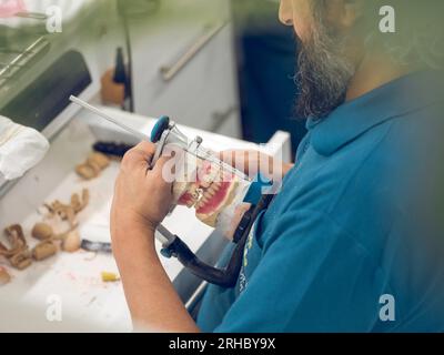 Du dessus de la vue latérale récolte technicien homme senior ajustant la prothèse de mâchoire dentaire dans l'articulateur tout en travaillant dans le laboratoire professionnel Banque D'Images