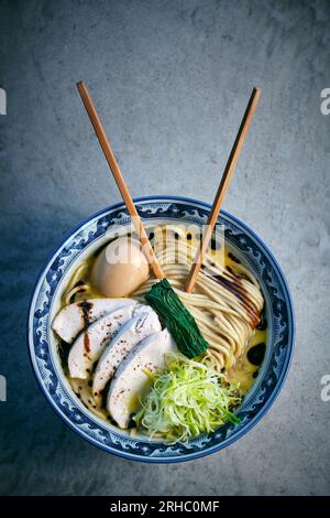 Vue de dessus d'une délicieuse soupe de nouilles japonaises avec des légumes frais et des œufs durs dans un bouillon avec des baguettes sur fond gris Banque D'Images