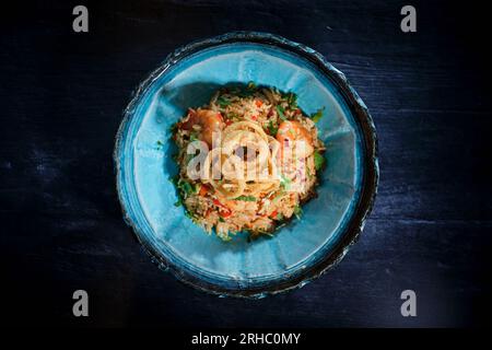 Vue de dessus de savoureux et délicieux riz frit avec crevettes herbes fraîches et légumes servis avec des anneaux de calmar dans un bol sur la table noire Banque D'Images